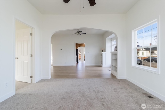 carpeted spare room featuring arched walkways, baseboards, and a ceiling fan