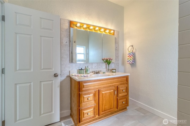 bathroom with visible vents, baseboards, vanity, and a textured wall