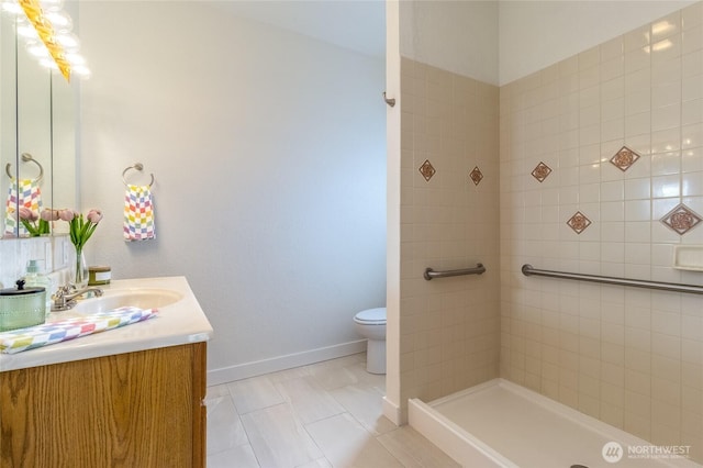 bathroom featuring vanity, toilet, baseboards, and a tile shower