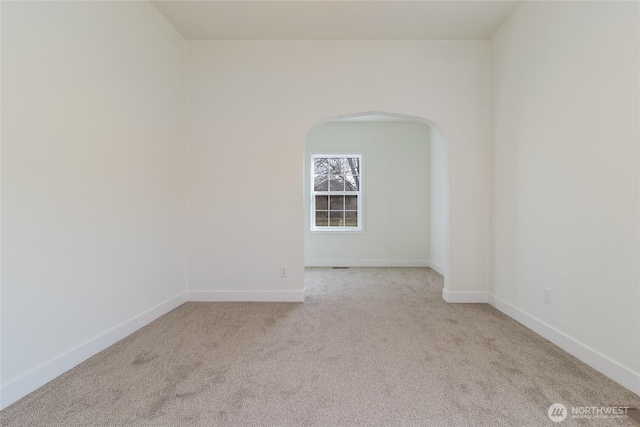 unfurnished room with arched walkways, baseboards, and carpet floors