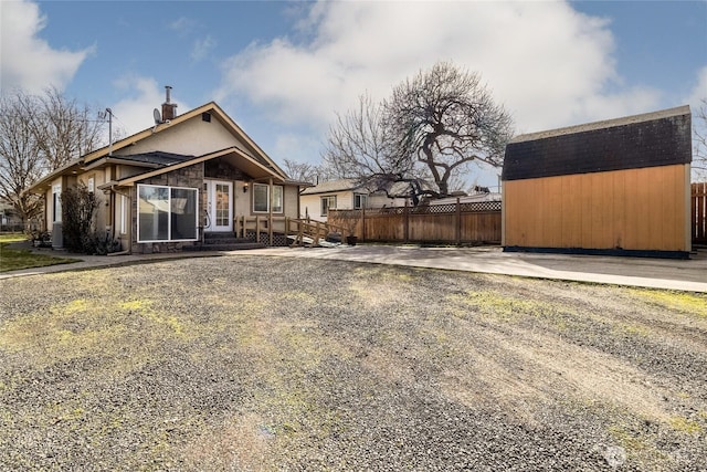 view of front of house featuring fence, a storage shed, an outdoor structure, stone siding, and driveway