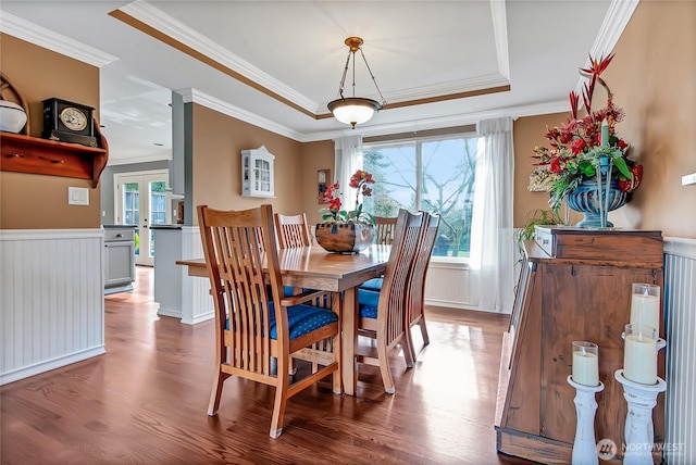 dining space with wood finished floors, a wainscoted wall, a tray ceiling, ornamental molding, and french doors