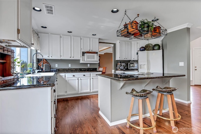 kitchen featuring visible vents, dark wood-type flooring, a sink, white appliances, and white cabinets