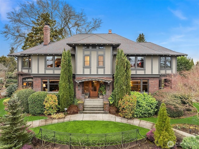 tudor house with a front lawn, a chimney, brick siding, and stucco siding