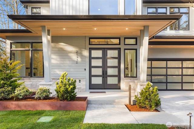 doorway to property with a garage, stone siding, board and batten siding, and covered porch