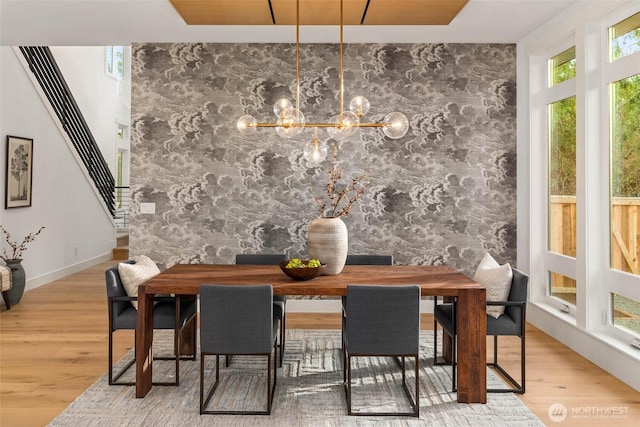 dining room featuring a chandelier, wood finished floors, an accent wall, and stairway