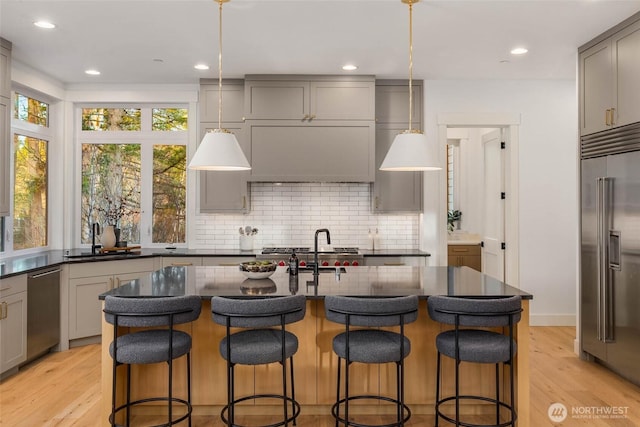 kitchen with light wood-style flooring, gray cabinets, a sink, decorative backsplash, and appliances with stainless steel finishes