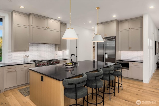 kitchen with stainless steel built in fridge, light wood-style flooring, a sink, dark countertops, and stove