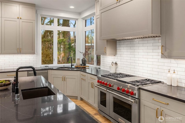 kitchen with range with two ovens, decorative backsplash, custom range hood, and a sink