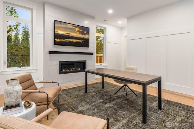 office featuring wood finished floors, recessed lighting, a large fireplace, a decorative wall, and a healthy amount of sunlight