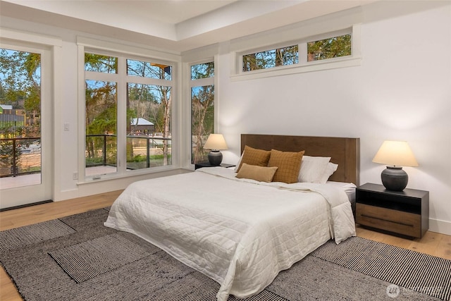 bedroom with access to outside, multiple windows, baseboards, and wood finished floors