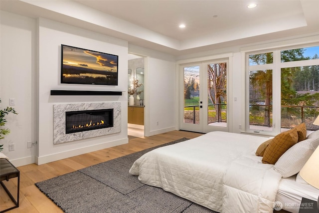 bedroom with access to outside, multiple windows, wood finished floors, and a premium fireplace