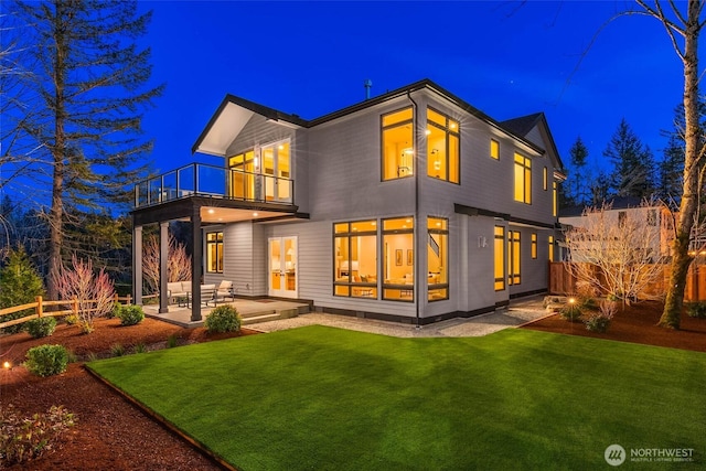 back of house at twilight with a lawn, a patio, a balcony, and fence