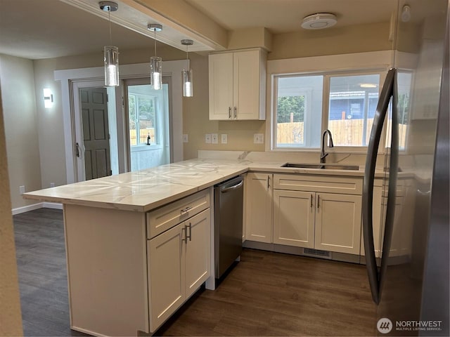 kitchen with a healthy amount of sunlight, a peninsula, a sink, white cabinets, and appliances with stainless steel finishes