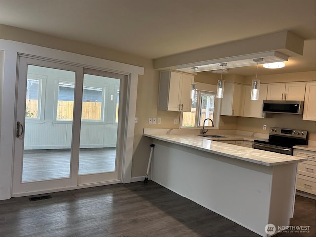 kitchen featuring visible vents, a sink, a peninsula, appliances with stainless steel finishes, and white cabinets