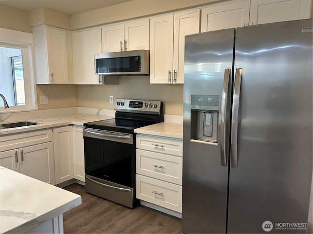 kitchen with light stone counters, a sink, stainless steel appliances, dark wood-type flooring, and white cabinetry