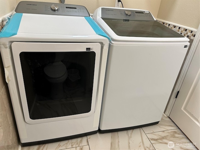 laundry area featuring washing machine and clothes dryer, marble finish floor, and a textured wall