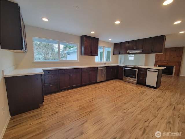 kitchen with a peninsula, stainless steel appliances, dark brown cabinetry, light countertops, and light wood-style floors