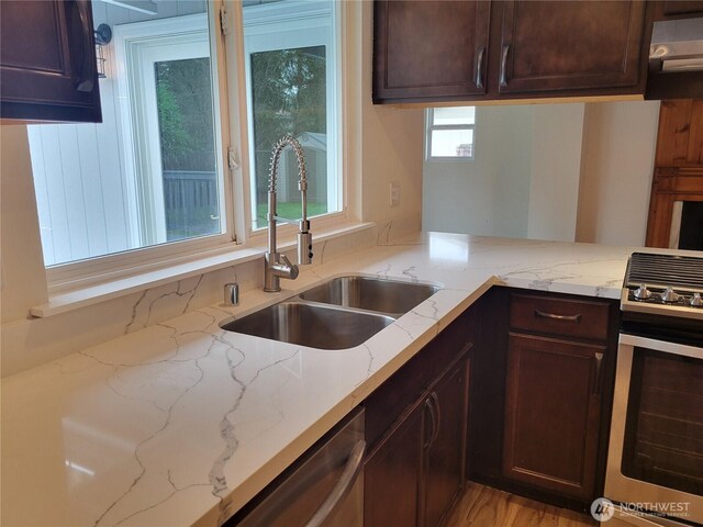 kitchen featuring a sink, dark brown cabinetry, light stone countertops, and stainless steel appliances