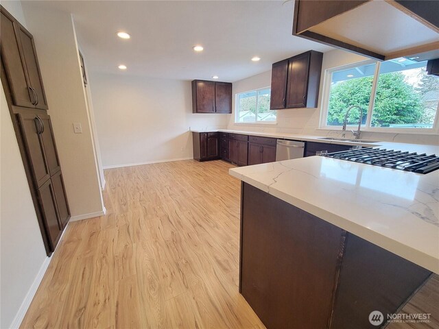 kitchen with light stone countertops, a sink, dark brown cabinets, dishwasher, and light wood-type flooring