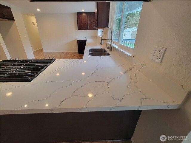 kitchen with a sink, light stone countertops, and dark brown cabinetry