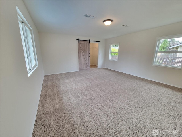 spare room featuring visible vents, light colored carpet, and a barn door