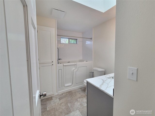 full bathroom with toilet, a tub to relax in, stone finish floor, a shower, and vanity