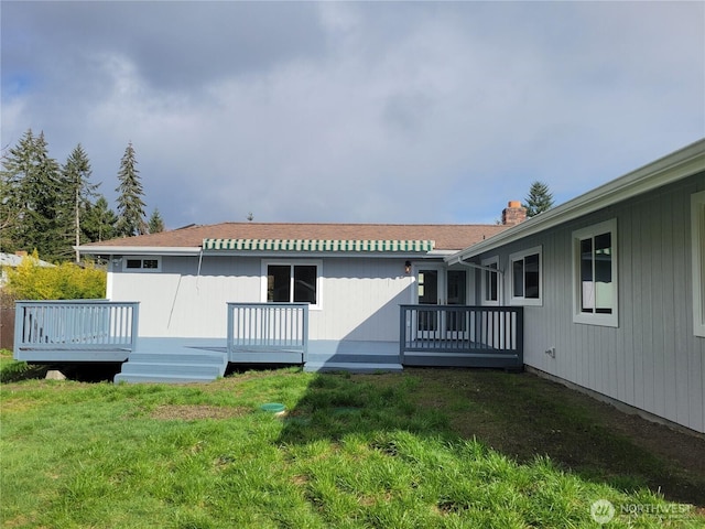 back of house featuring a chimney, a lawn, and a wooden deck