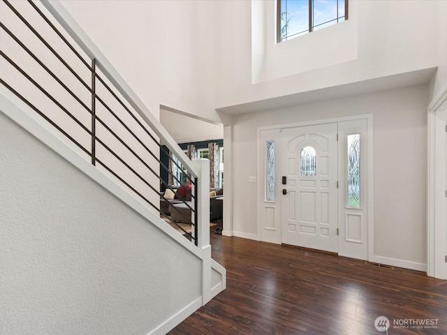 entryway featuring a towering ceiling, stairs, baseboards, and wood finished floors