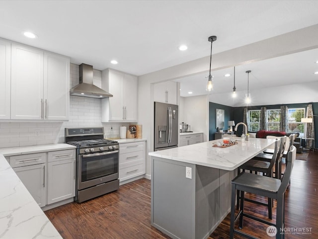 kitchen featuring dark wood-style floors, decorative backsplash, stainless steel appliances, and wall chimney exhaust hood