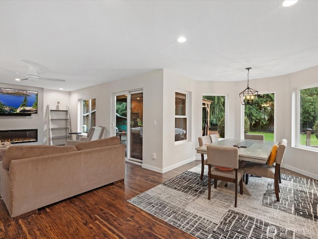 dining room featuring baseboards, dark wood finished floors, recessed lighting, ceiling fan with notable chandelier, and a glass covered fireplace