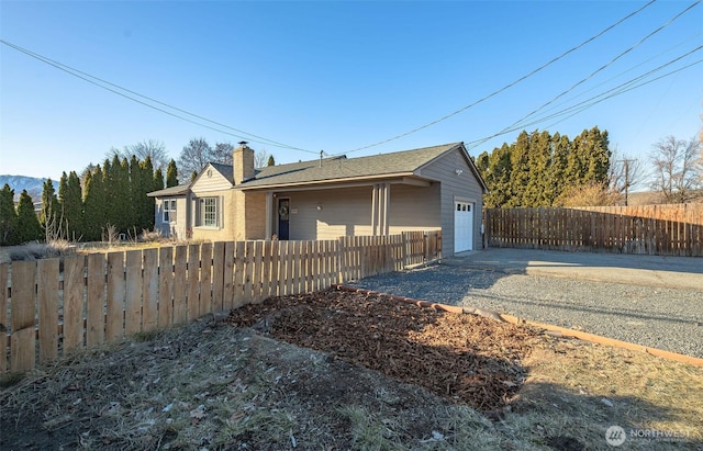 view of property exterior with a fenced front yard, concrete driveway, a chimney, and a garage