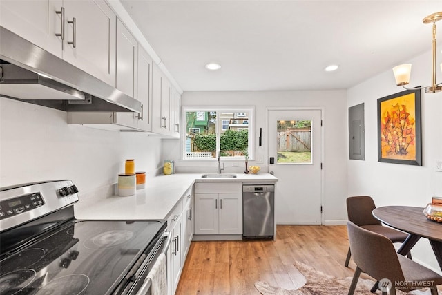 kitchen featuring light wood-style flooring, under cabinet range hood, a sink, appliances with stainless steel finishes, and light countertops