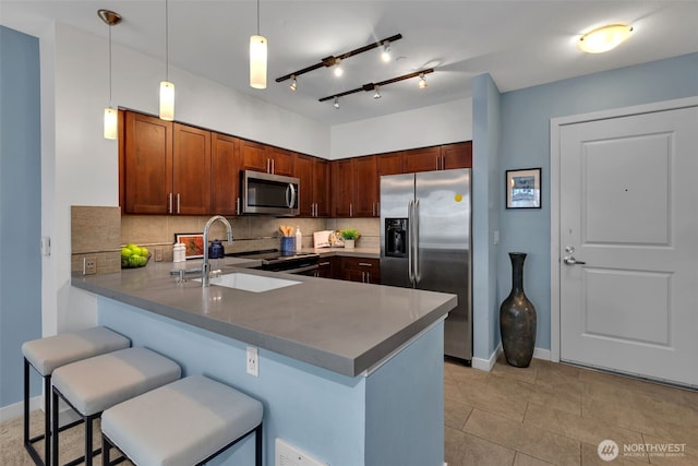 kitchen featuring a sink, a kitchen breakfast bar, stainless steel appliances, a peninsula, and decorative backsplash