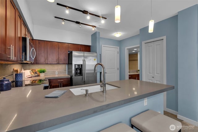 kitchen with pendant lighting, decorative backsplash, appliances with stainless steel finishes, a peninsula, and a sink