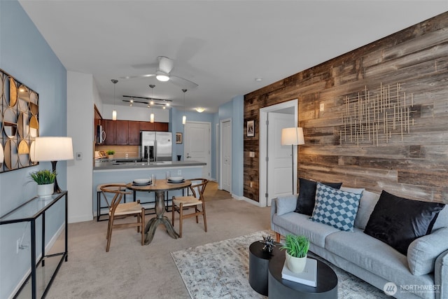 living room with wooden walls, a ceiling fan, baseboards, rail lighting, and light carpet