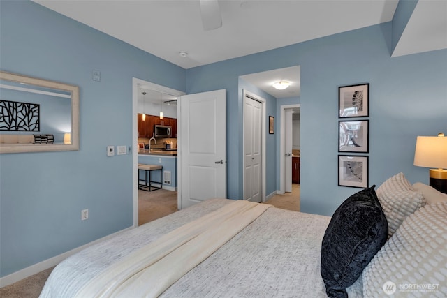 bedroom featuring a ceiling fan, a sink, a closet, carpet flooring, and baseboards