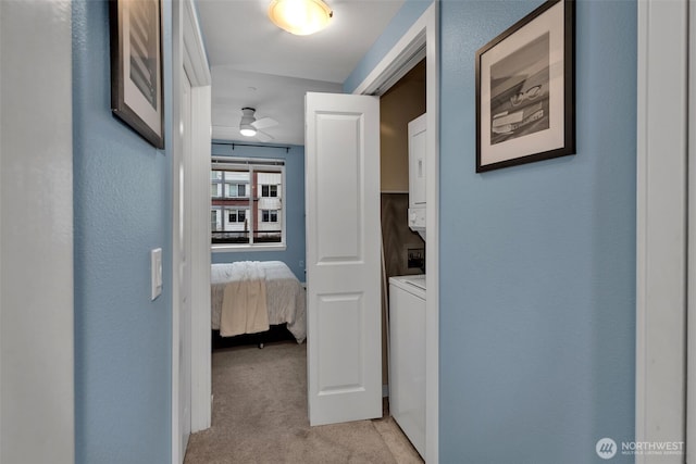 hall with stacked washer / dryer, light colored carpet, and a textured wall