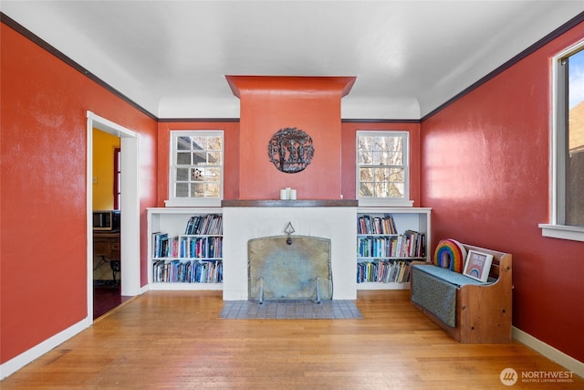 unfurnished living room with a fireplace with flush hearth, wood finished floors, baseboards, and ornamental molding