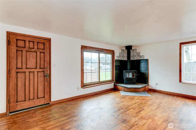 unfurnished living room featuring baseboards, light wood-style floors, and a wood stove