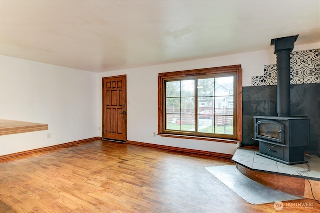 unfurnished living room featuring a wood stove, baseboards, and wood finished floors