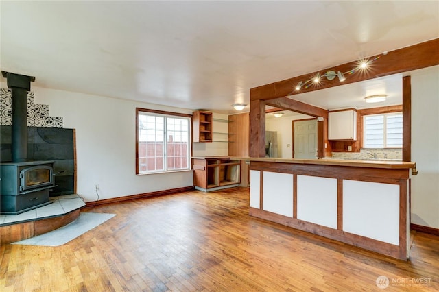 unfurnished living room with a wood stove, light wood-style floors, and baseboards