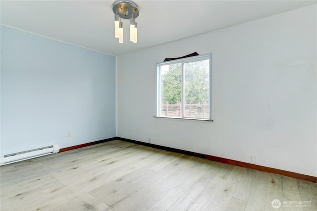 empty room featuring a baseboard heating unit, baseboards, and light wood finished floors