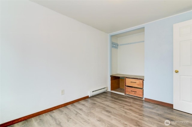 unfurnished bedroom featuring a baseboard heating unit, baseboards, and light wood-type flooring