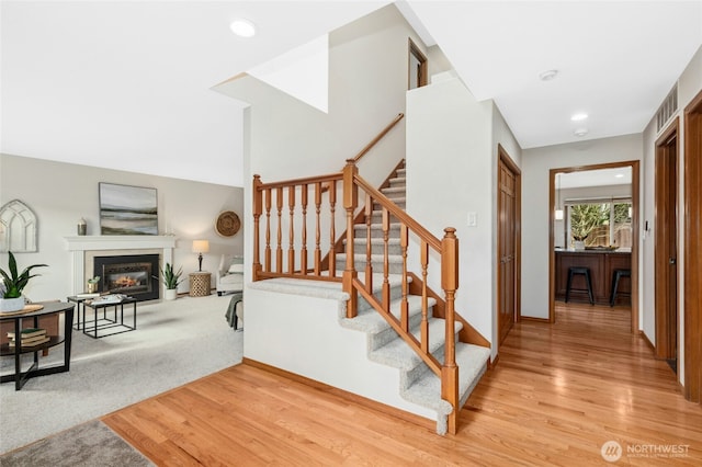 stairs featuring recessed lighting, visible vents, wood finished floors, and a glass covered fireplace