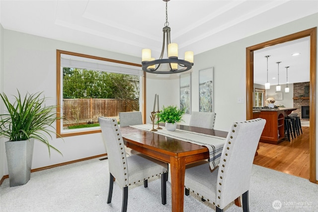 dining room featuring baseboards, light colored carpet, light wood-type flooring, a tray ceiling, and an inviting chandelier