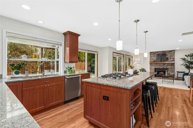 kitchen with a sink, light stone counters, a kitchen breakfast bar, stainless steel appliances, and light wood finished floors