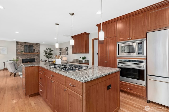 kitchen with light wood finished floors, a kitchen island, a fireplace, stainless steel appliances, and open floor plan