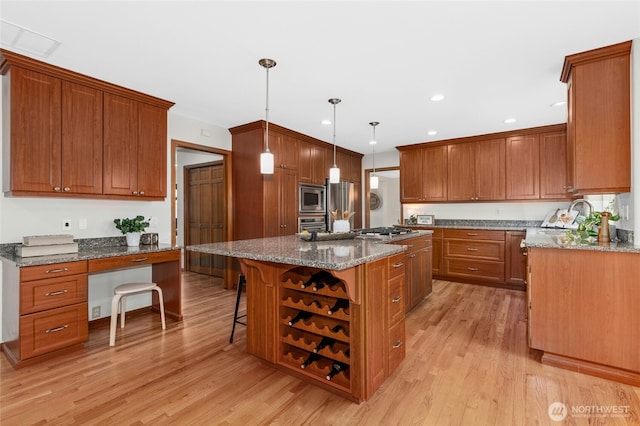 kitchen featuring light wood-type flooring, a center island, stainless steel appliances, dark stone counters, and brown cabinetry