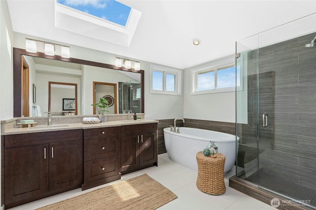 bathroom with a soaking tub, a skylight, double vanity, a sink, and a shower stall